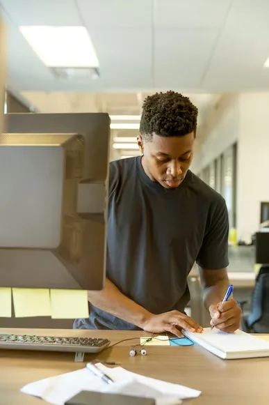 Student taking notes at a computer desk